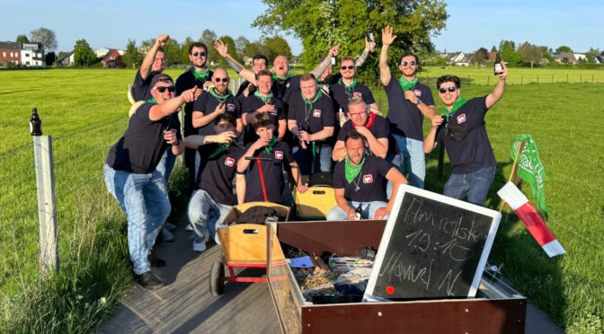 Eine Gruppe junger Männer auf einem Feldweg feiern mit Bollerwagen